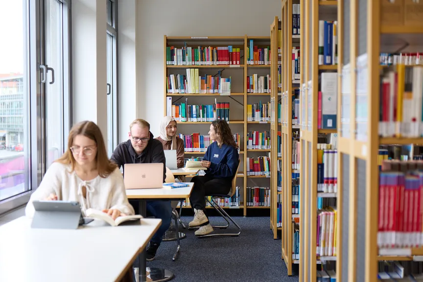 Einige Studierende sitzen an Arbeitsplätzen in einer Bibliothek und arbeiten