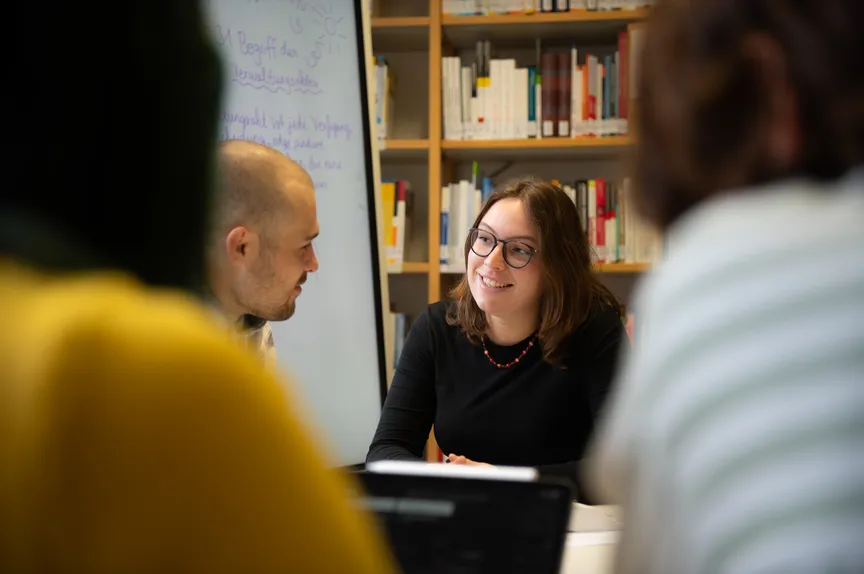 Eine Gruppe Studierender macht eine Gruppenarbeit in einer Bibliothek, zwei Personen unterhalten sich