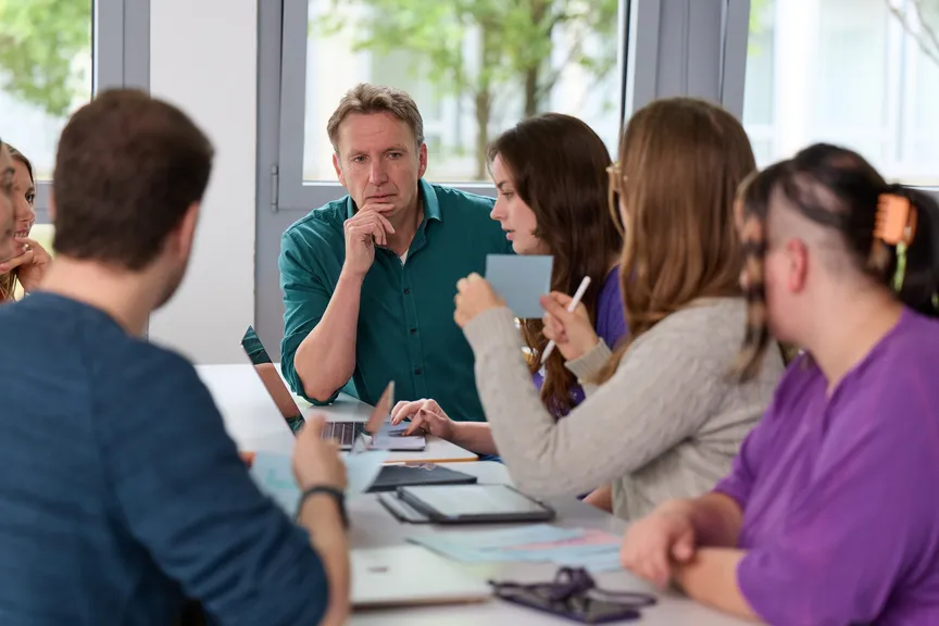 Eine Gruppe Studierender arbeitet miteinander in einem Seminar und unterhält sich mit einem Dozenten
